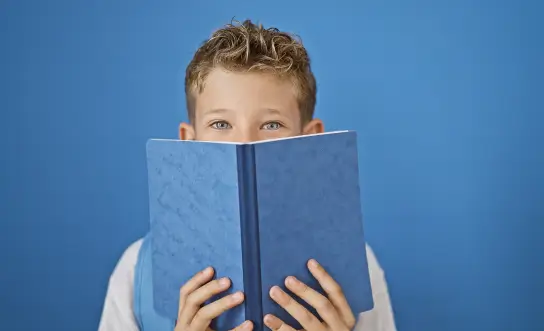 a young boy holding a blue book over his face